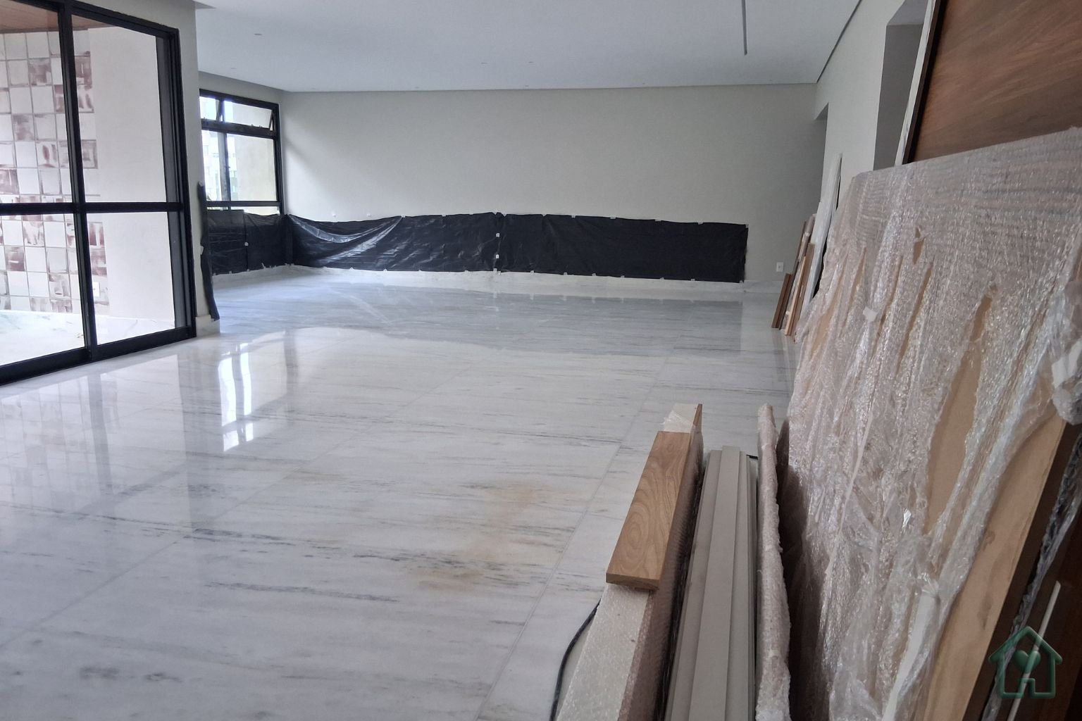 Sala ampla recém-reformada com piso de porcelanato claro e marcenaria protegida por plástico bolha, aguardando o início da limpeza pós-obra.